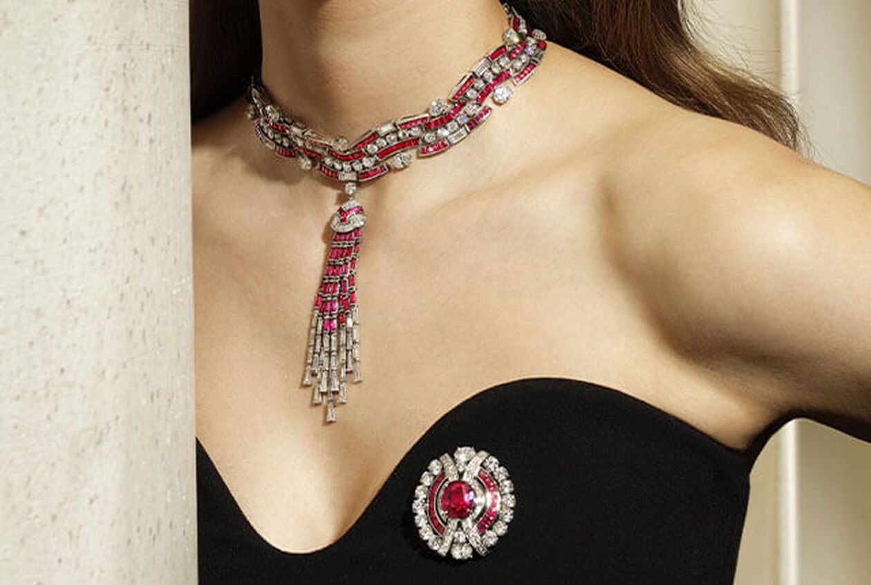 Modelo luciendo una gargantilla Magnifica de Alta Joyería en platino con borla, con diamantes y rubíes engastados sobre un fondo blanco con el logotipo de Bvlgari.